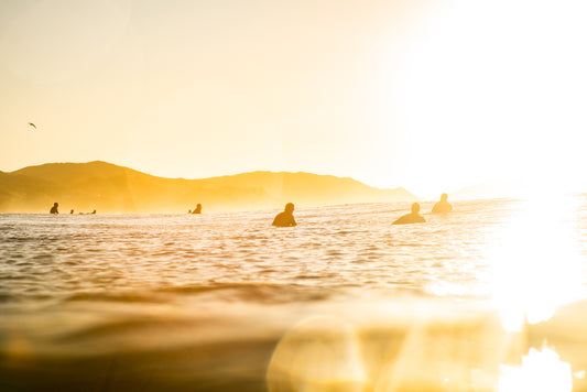 Group of surfers sitting around in the surf at sunrise at Wainui Beach in Gisborne