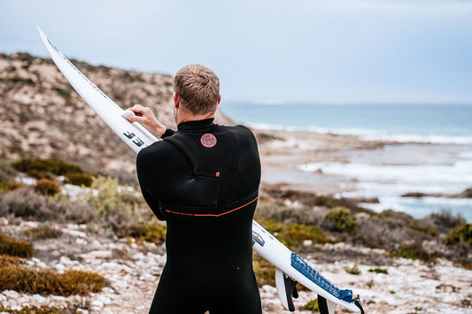 Mick Fanning holding his surfboard in a winter wetsuit