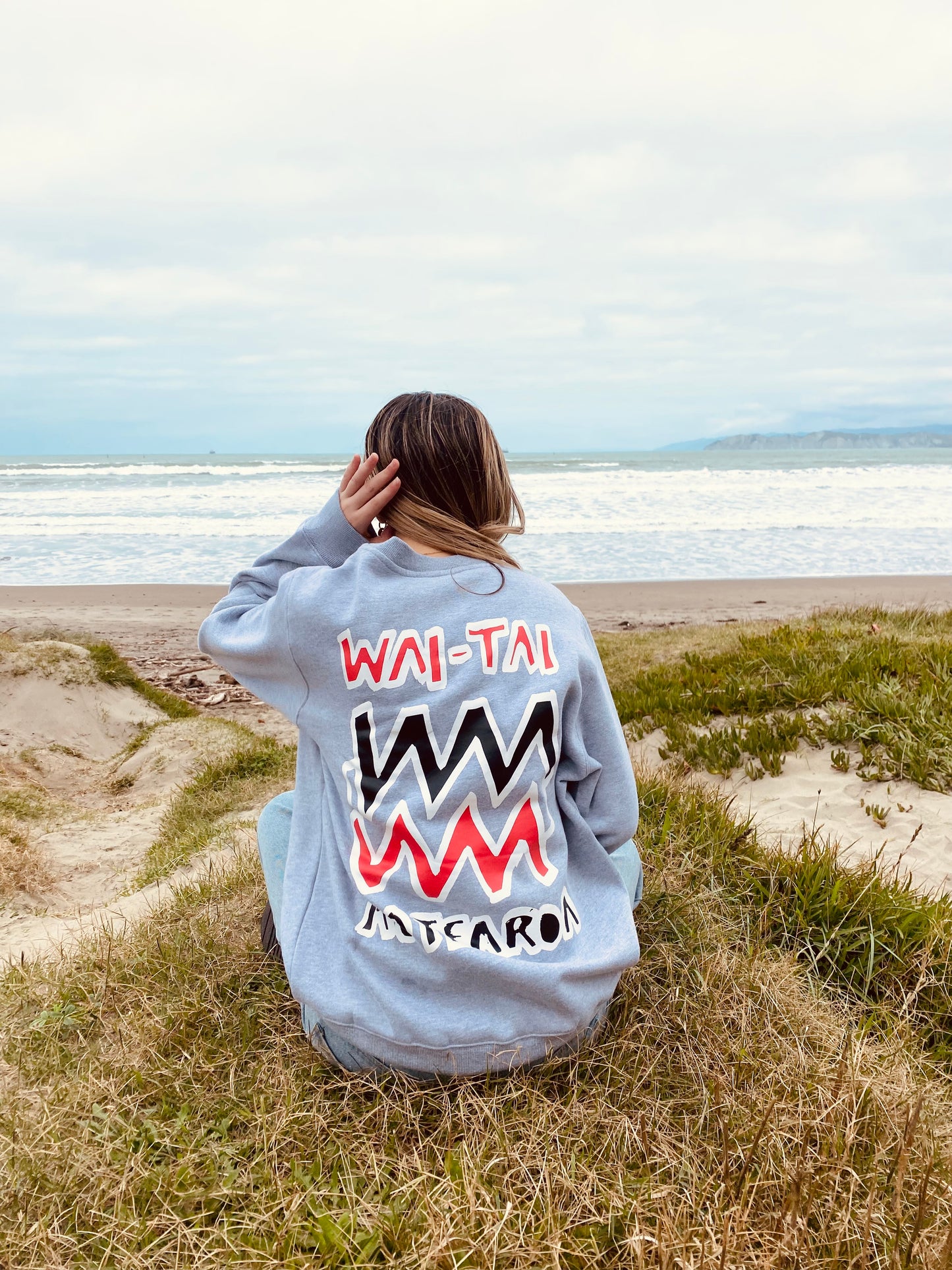 Wai-Tai Aotearoa Mura Crew in grey marle from rear on seated model at Midway Beach in Gisborne