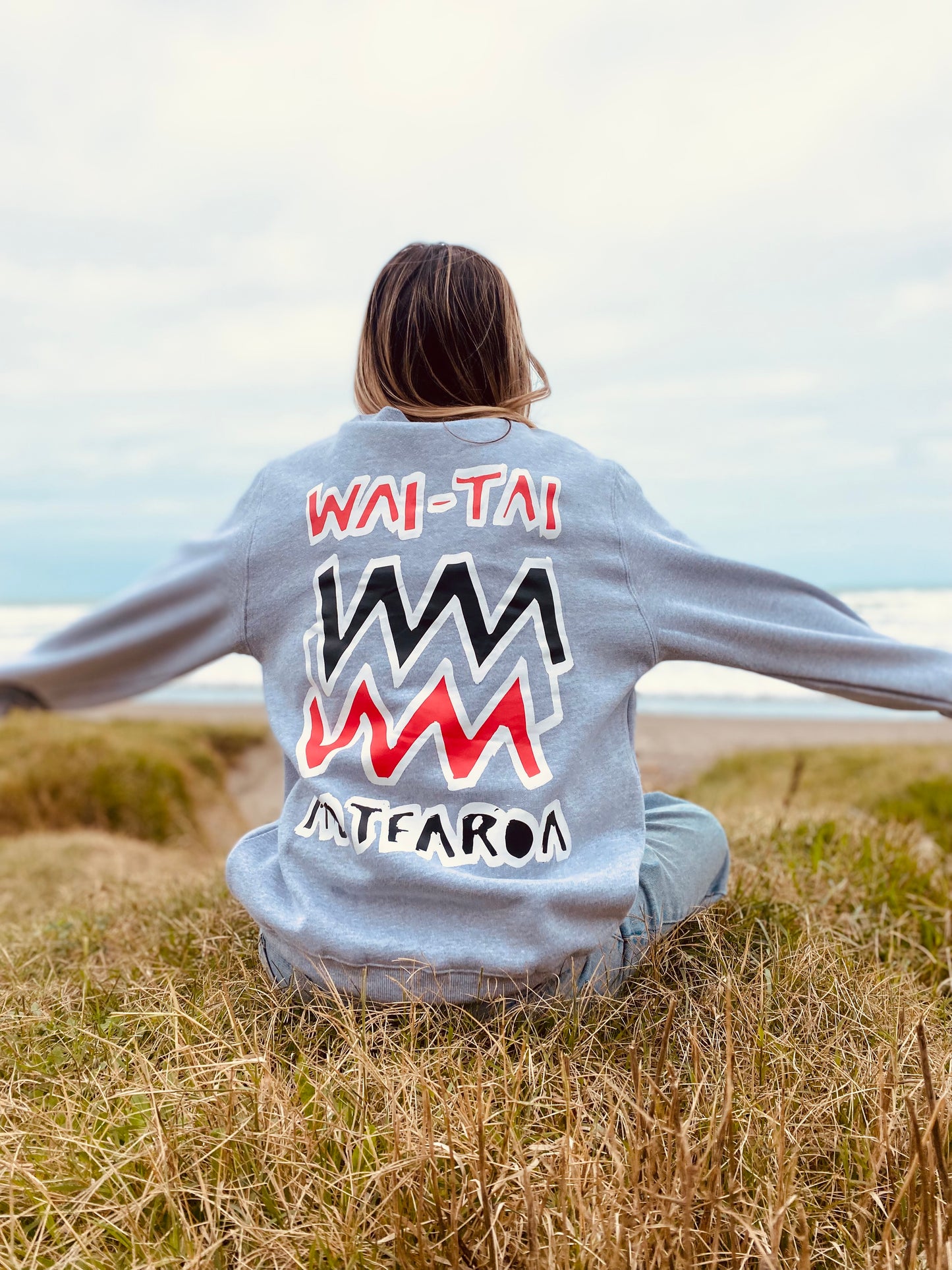 Wai-Tai Aotearoa Mura Crew in grey marle from rear with arms outstretched on model at Midway Beach in Gisborne