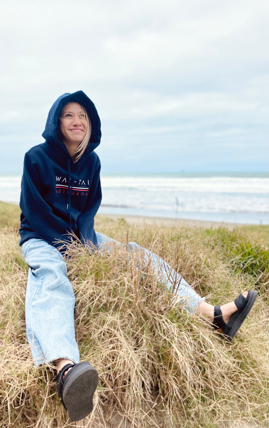 Wai-Tai Taniwha Maori Hoodie in navy from front view on model sitting at Midway Beach