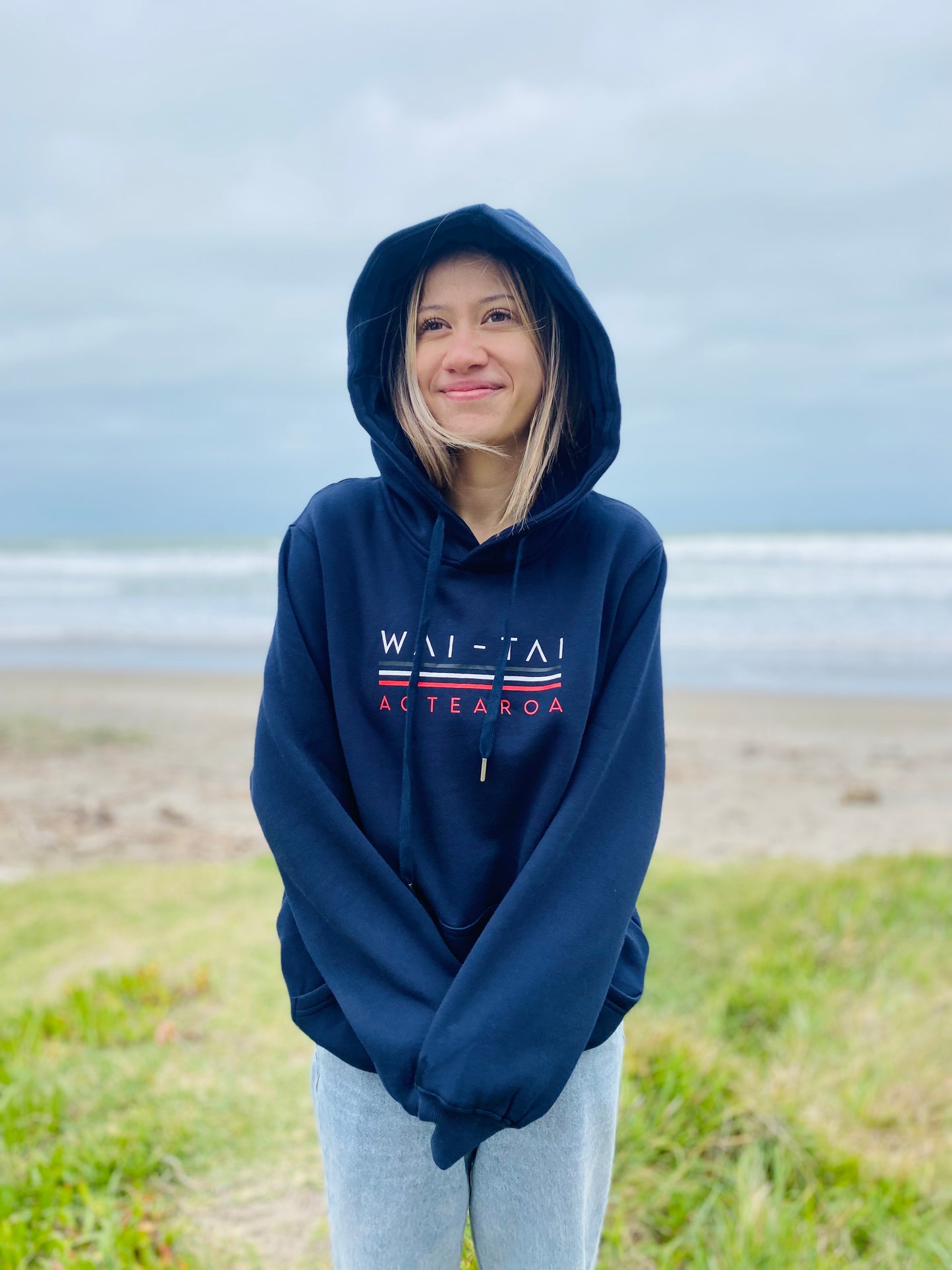 Wai-Tai Aotearoa Taniwha Maori Hoodie in navy colour from front on model at Midway Beach in Gisborne