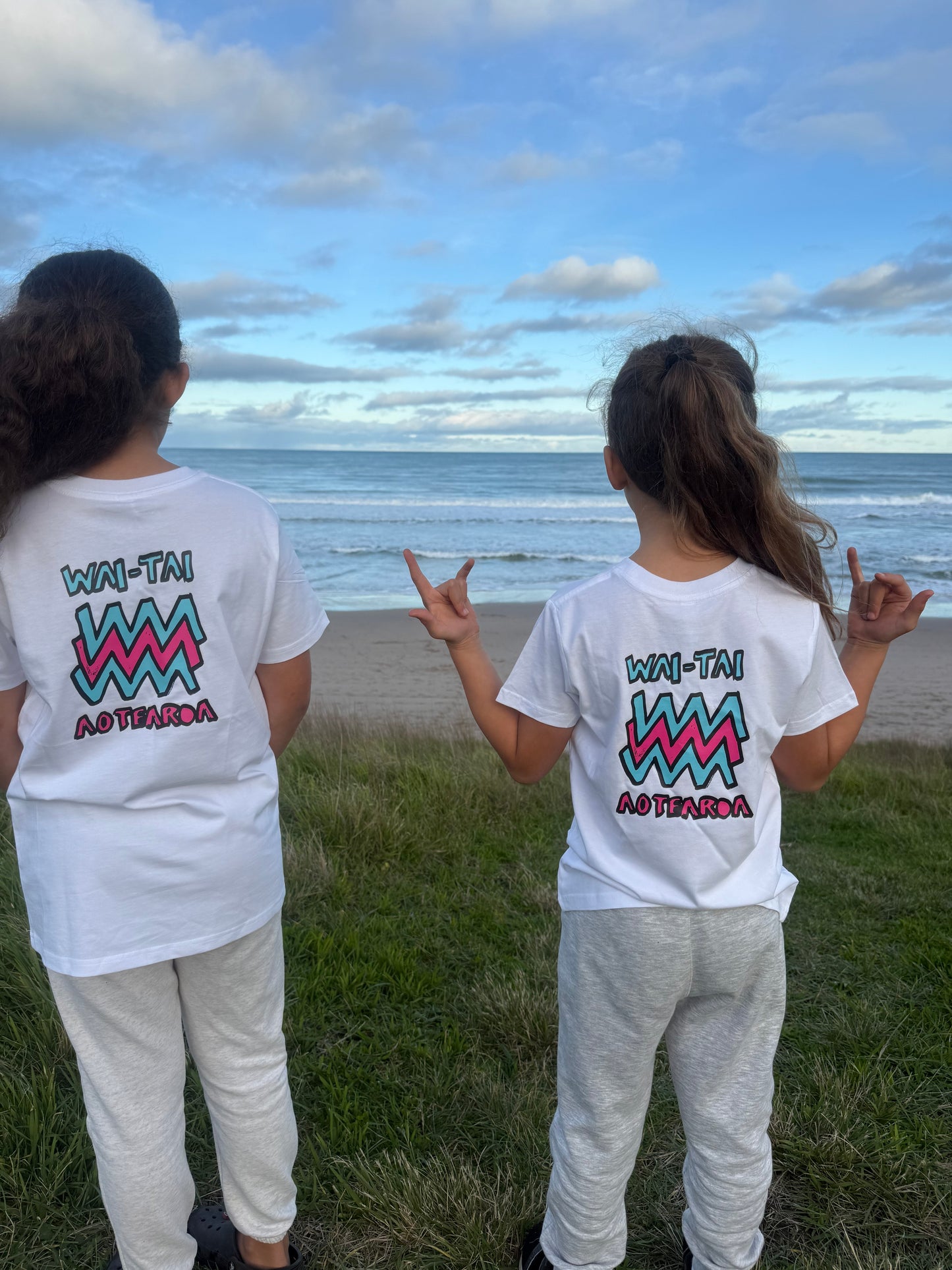 Wai-Tai Kids Mura Maori t-shirt in white from rear view at Okltu beach in Gisborne on two tamariki