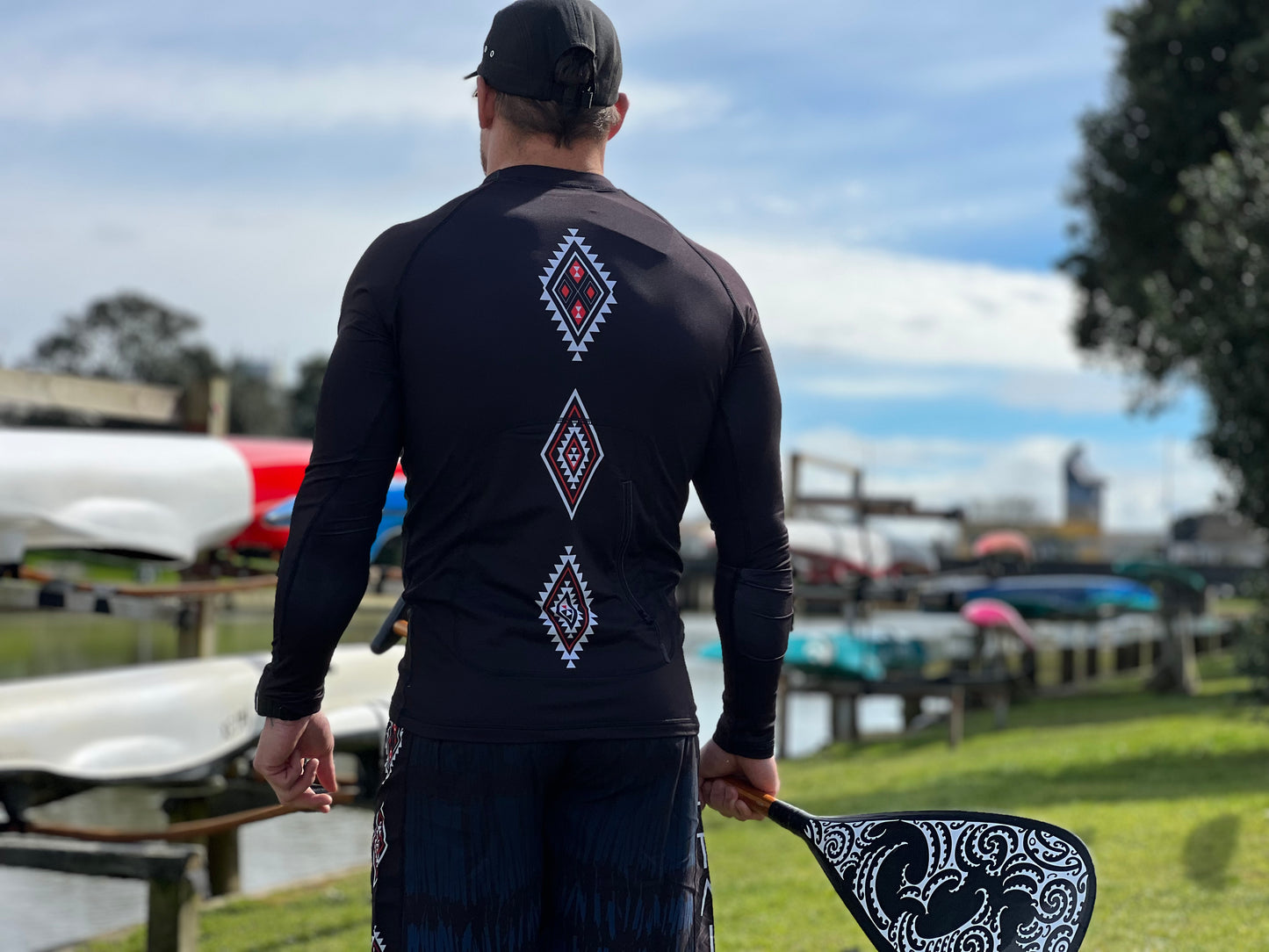 Wai-Tai Aotearoa Patiki Thermal Longsleeve Rash Top on Maia Gibbs holding a waka paddle from rear view