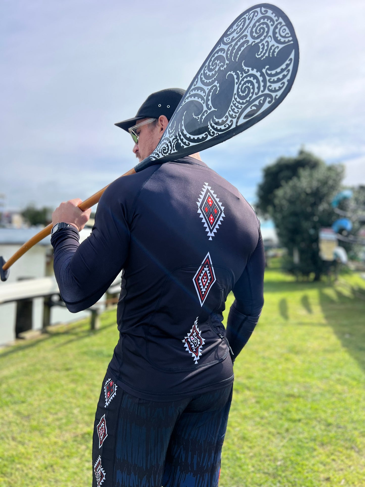 Wai-Tai Aotearoa Patiki Thermal Longsleeve Rash Top on Maia Gibbs holding a waka paddle from rear view