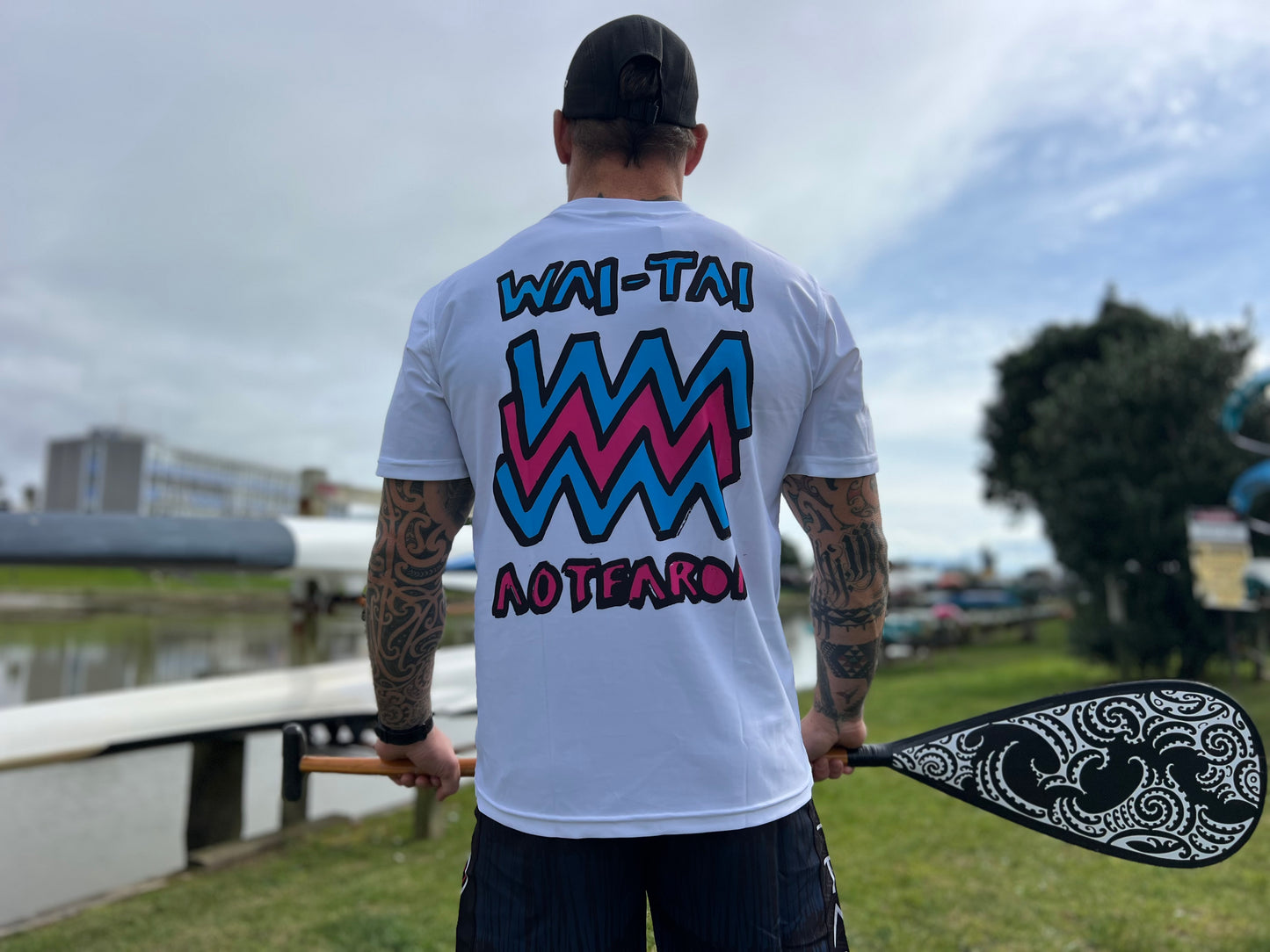 Wai-Tai Aotearoa Mura Rash Tee in white on Maia Gibbs holding a paddle in Gisborne from the back view