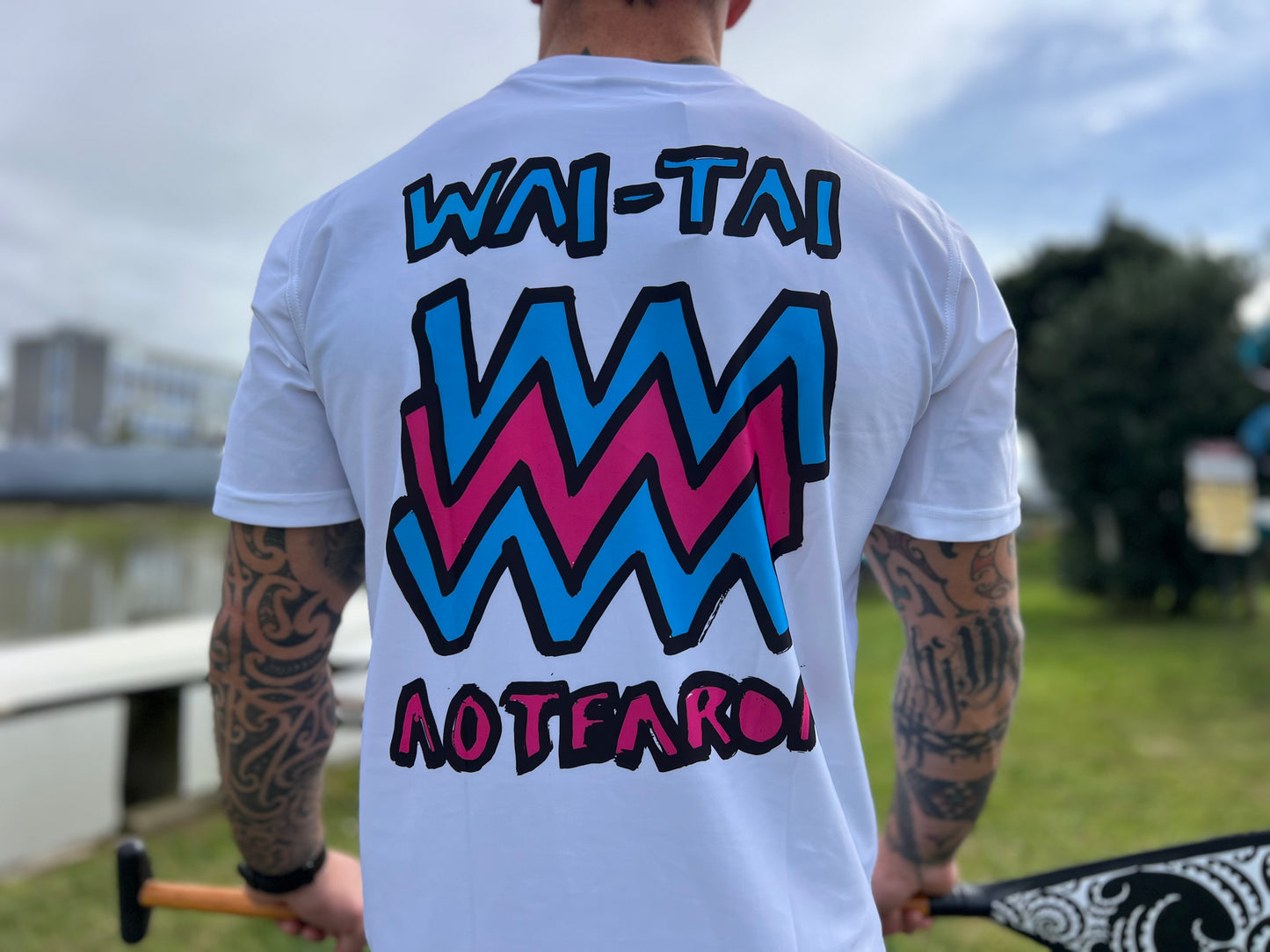 Wai-Tai Aotearoa Mura Rash Tee in white on Maia Gibbs holding a paddle in Gisborne from the back view close up
