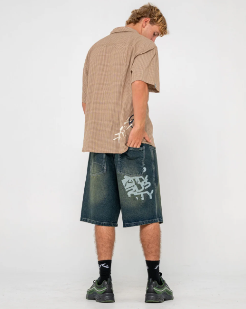 Rusty Stone Cold Baggy 24" Men's Denim Shorts in dark n dirty colourway from rear on model in tan shirt
