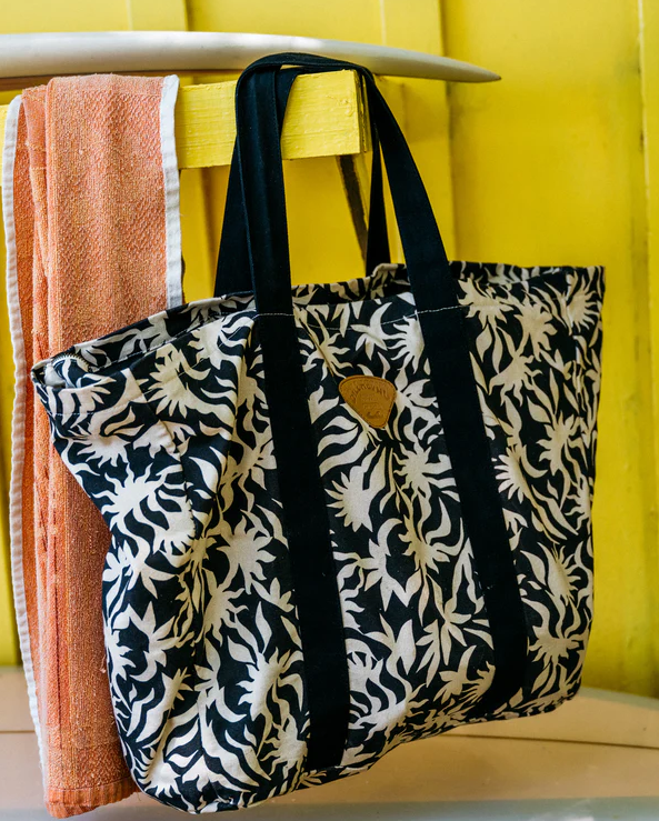 Billabong Poppins Playa Tote Bag in black and white floral print hanging from a surfboard with yellow background
