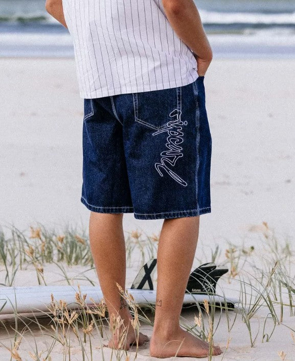 Rip Curl Medina Script 22" Denim Shorts from the rear showing embroidered rip curl sign on model at the beach