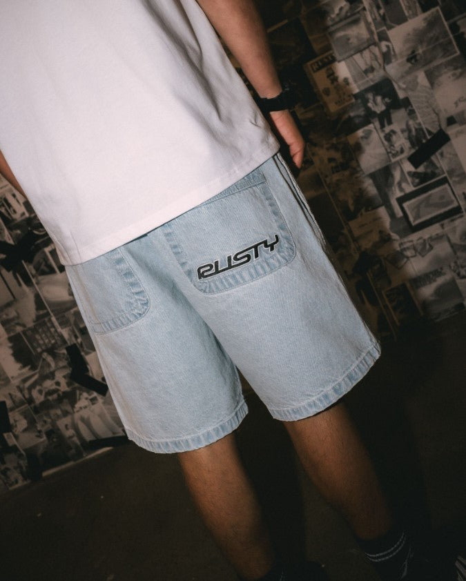 Rusty Flip Daddy 2.0 Denim Shorts in sky blue colourway in lifestyle shot on model with news clipping background from rear