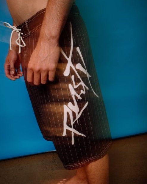 Rusty Hoodus Fixed Waist 23" Boardshorts in striped carbon colour in blurred out lifestyle image with blue background