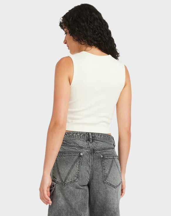 Person wearing a white sleeveless top and gray jeans on a plain background