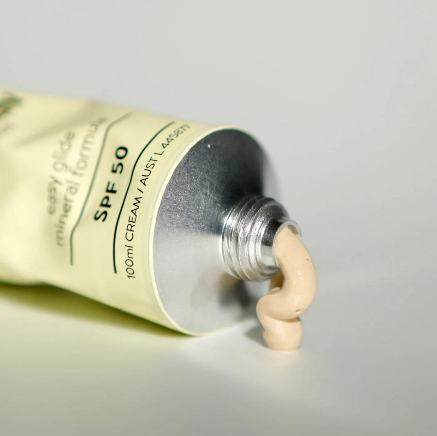 Tube of cream with a visible amount of cream being squeezed out on a neutral background
