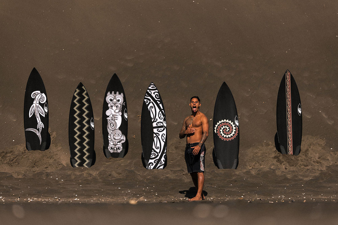 Kehu Butler in his Quiksilver maori boardshorts showing his surfboards standing in the stand