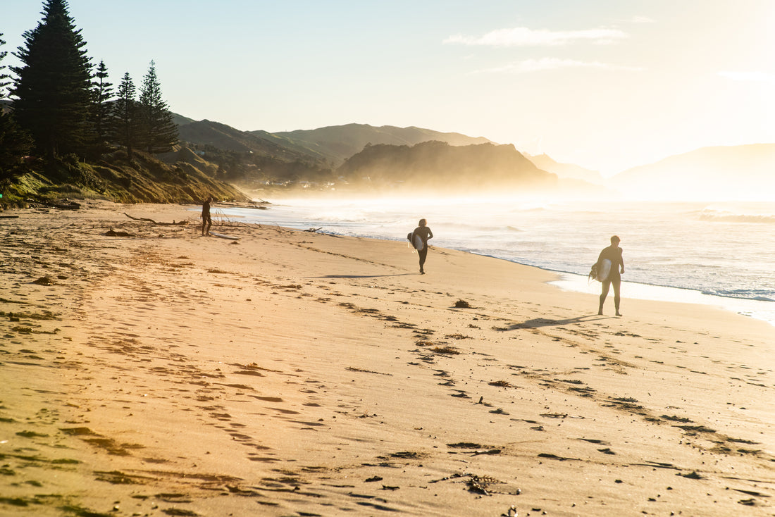 Surfers walking along Wainui Beach in Gisborne with their surfboards NZ