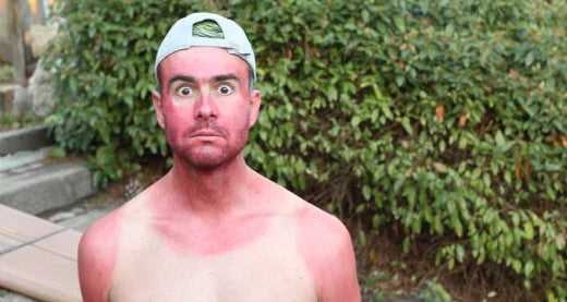 Very sunburnt person standing outside in cap