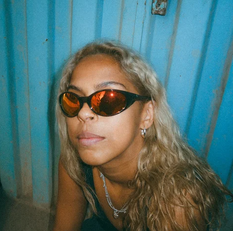 CHPO Brand Nori Unisex Sunglasses in coffee colourway with red ion lenses on female model outside a metal container