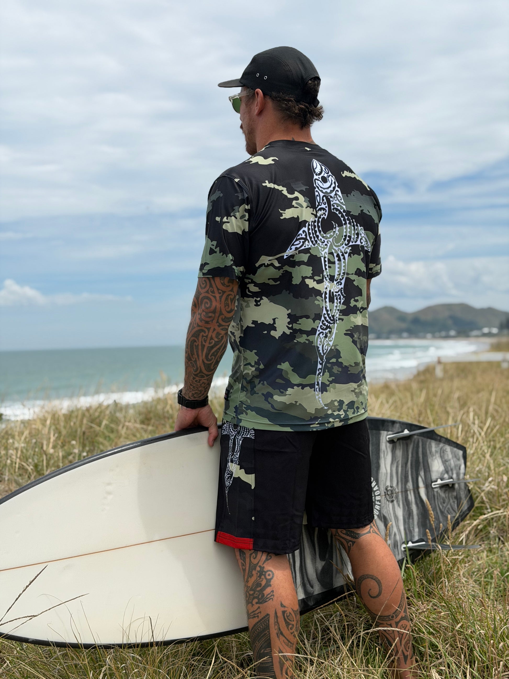 Wai-Tai Aotearoa Kaitiaki Black Camo 19" Tech Maori Design Boardshorts opn Maia Gibbs in camo rashie at Wainui Beach
