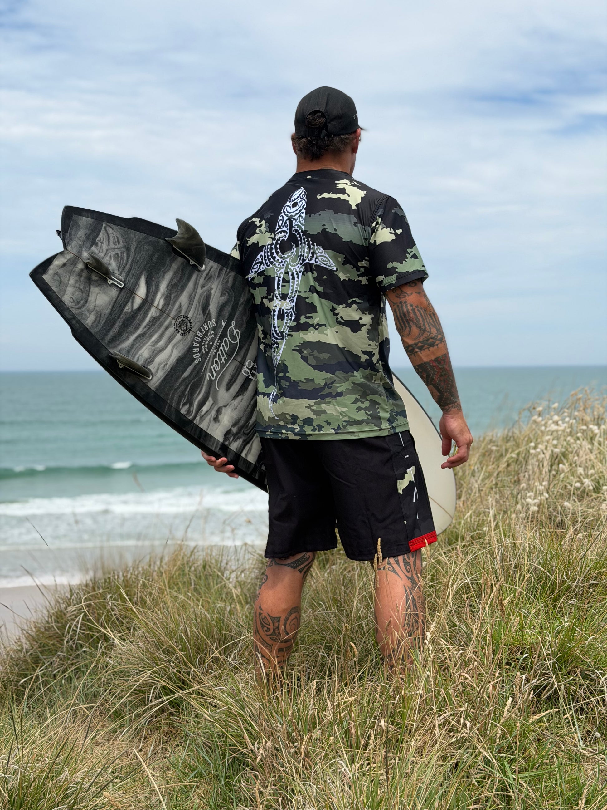 Wai-Tai Aotearoa Kaitiaki Camo Maori Design Shark Rash Tee on Hine Brooking holding a surfboard from rear view