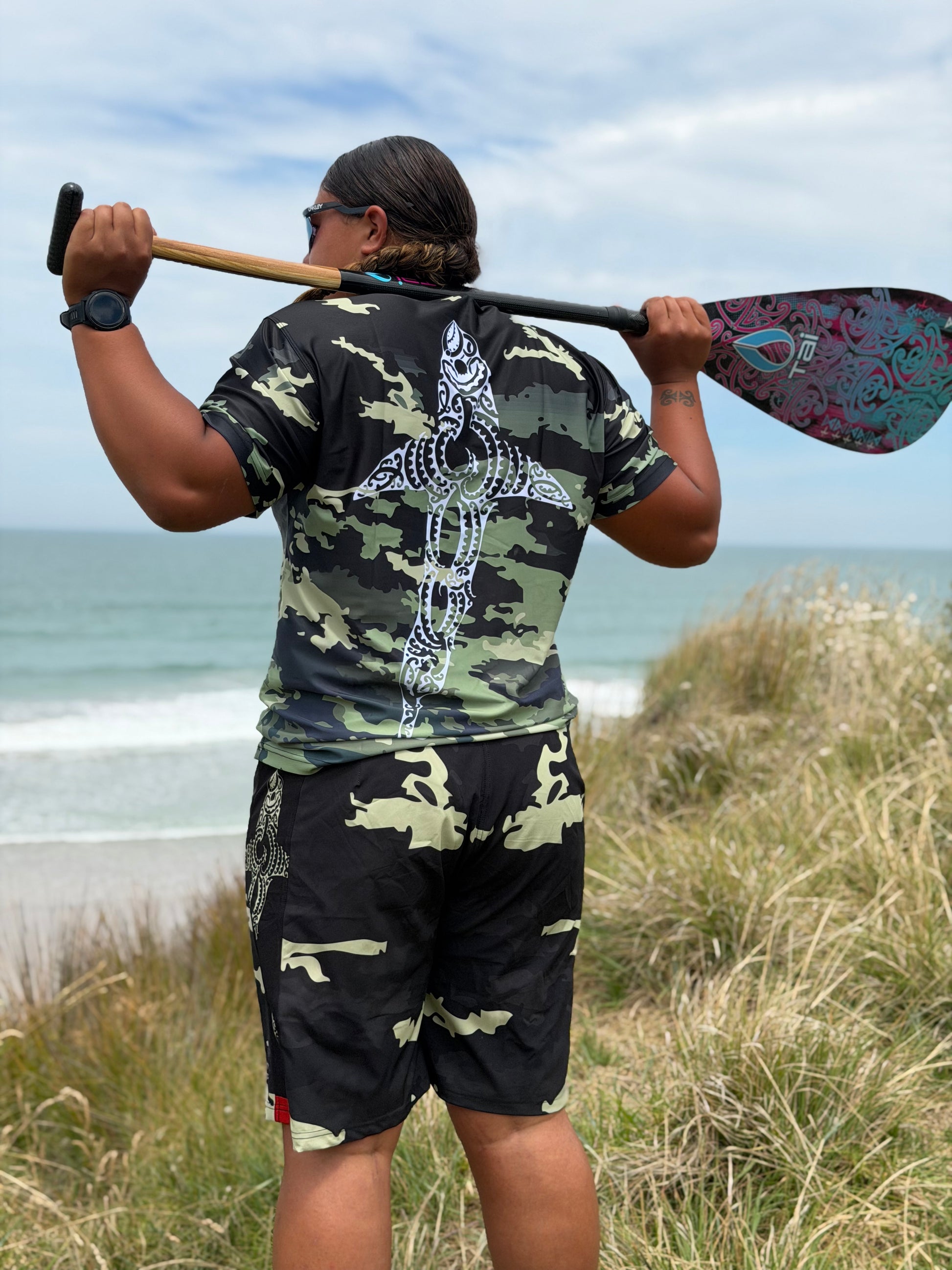 Wai-Tai Aotearoa Kaitiaki Yellow Camo 19" Tech Boardshorts from rear on Hine Brooking holding a paddle
