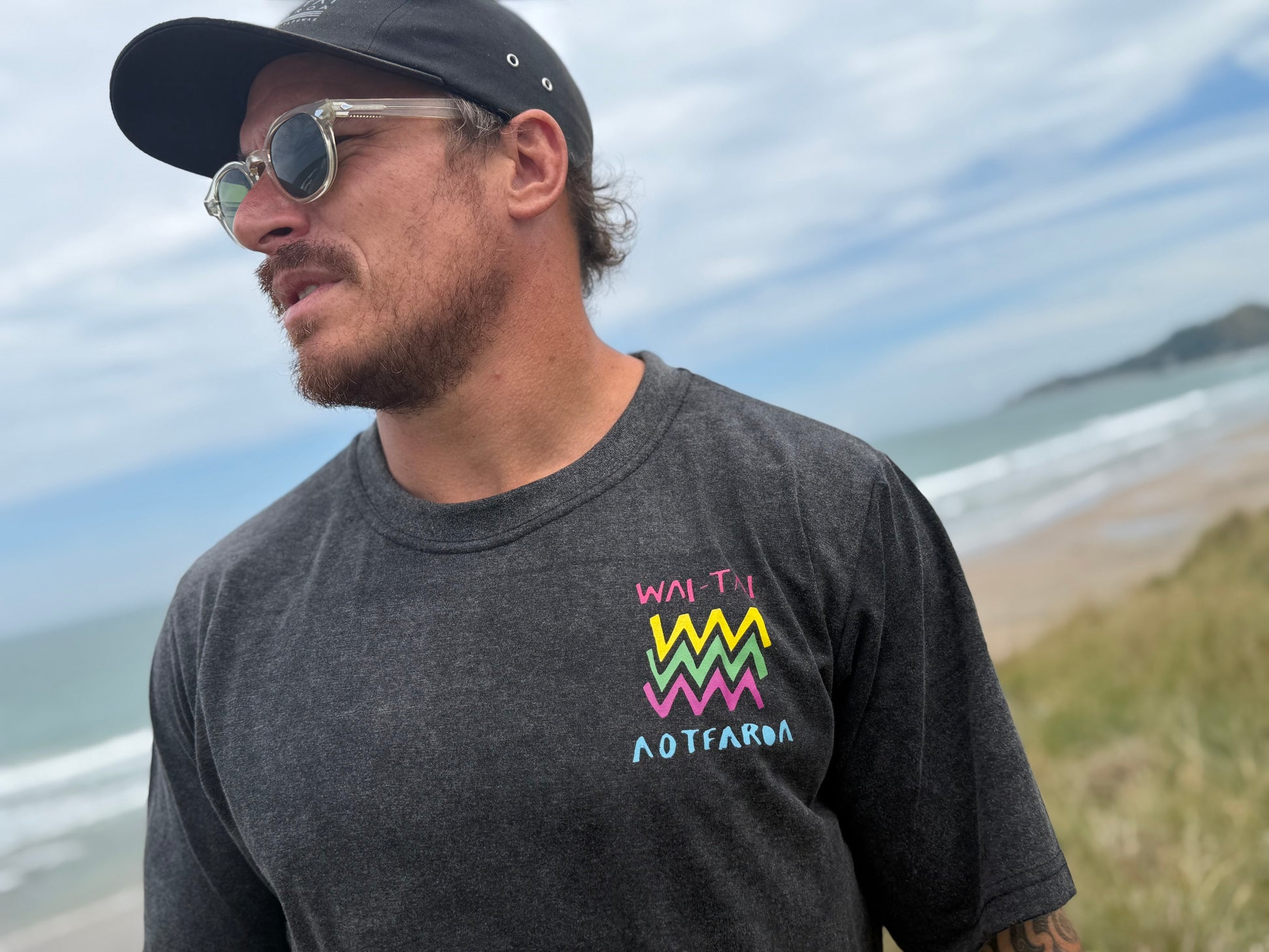 Wai-Tai Aotearoa Ono Whitu Unisex Stonewash Tee from front showing bright coloured logo on Maia Gibbs