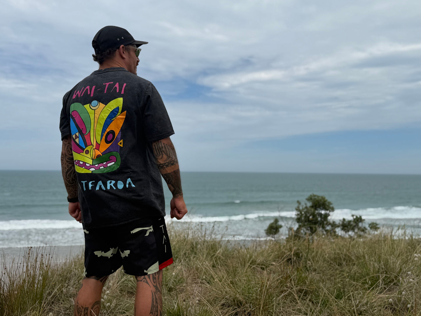 Wai-Tai Aotearoa Kaitiaki Yellow Camo 19" Tech Boardshorts from rear on Maia Gibbs wearing Ono Whitu tee at the beach