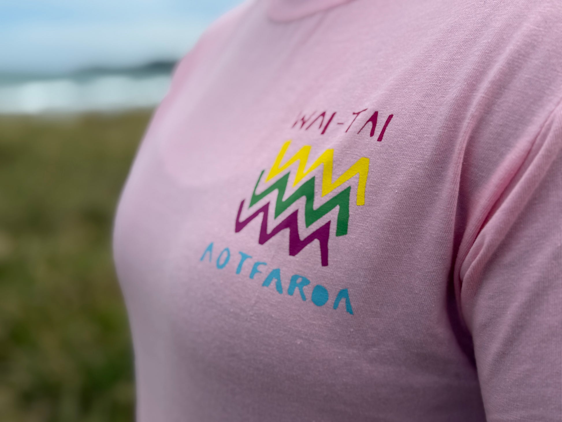 Wai-Tai Aotearoa Ono Whitu Pink Unisex Tee from frontshowing bright logo on Hine Brooking at the beach