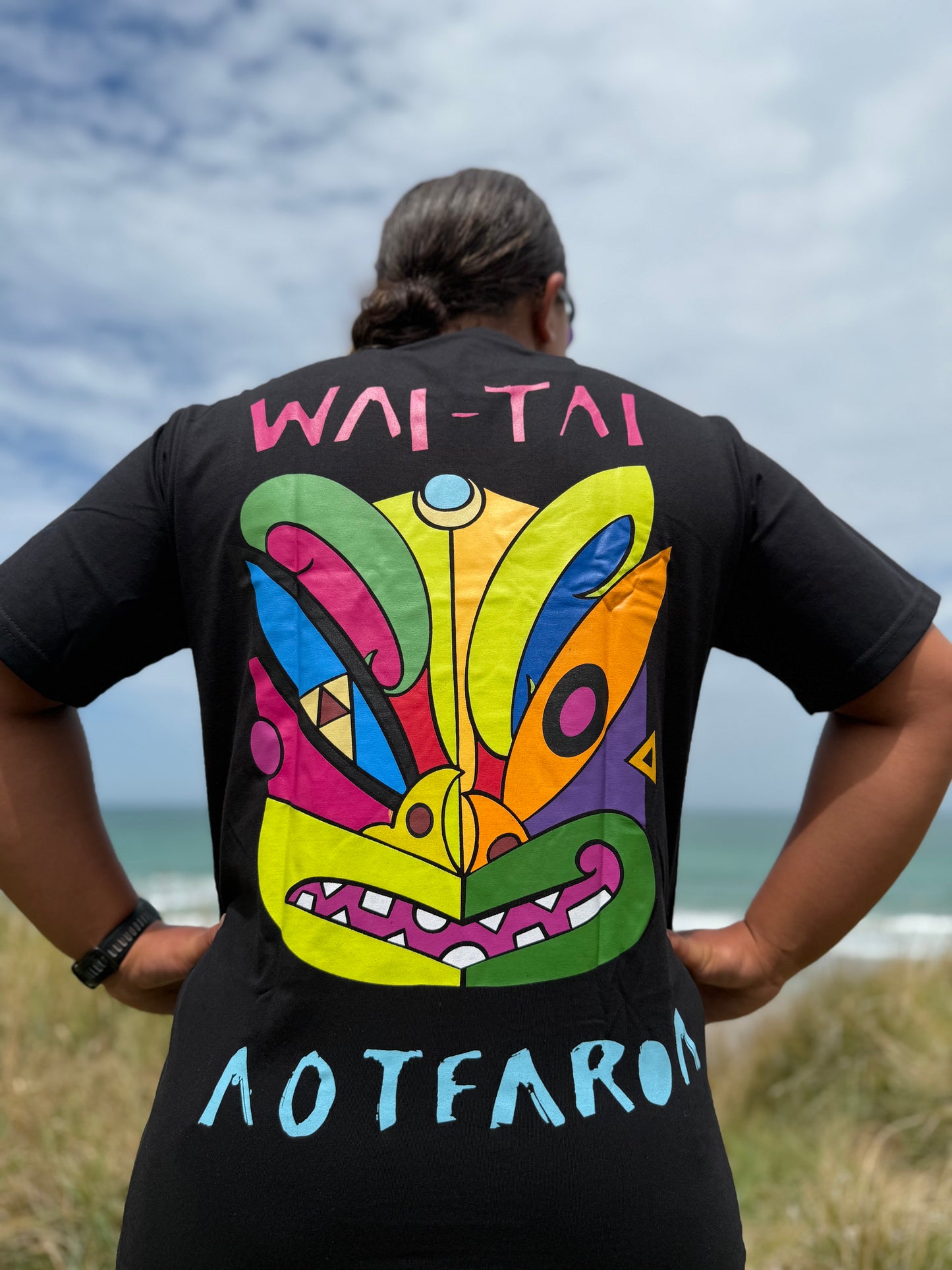 Wai-Tai Aotearoa Ono Whitu Black Unisex Maori Design T-Shirt in black worn by Hine Brooking showing bright tiki design from rear