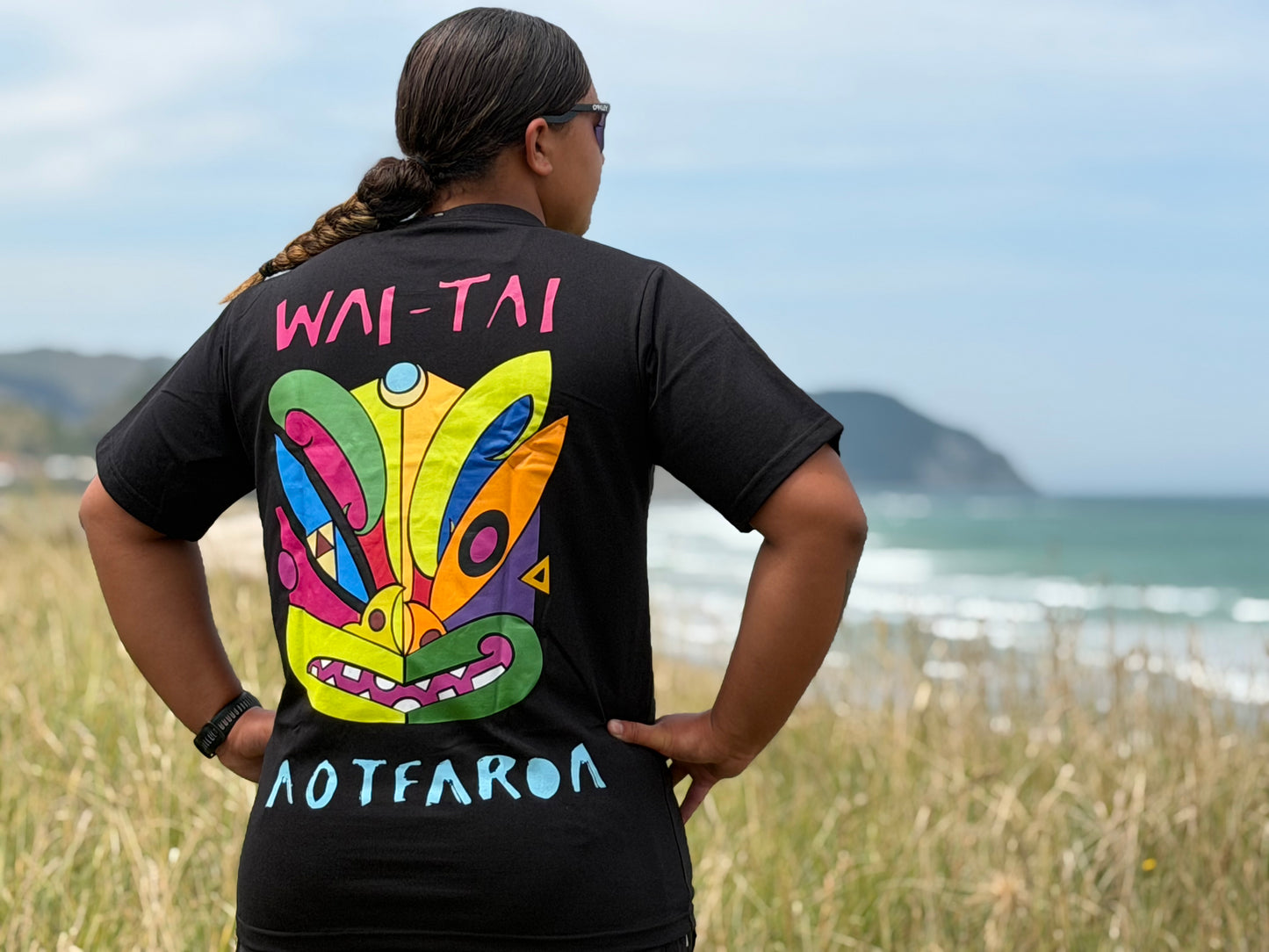 Wai-Tai Aotearoa Ono Whitu Black Unisex Maori Design T-Shirt in black worn by Hine Brooking showing bright tiki design from rear