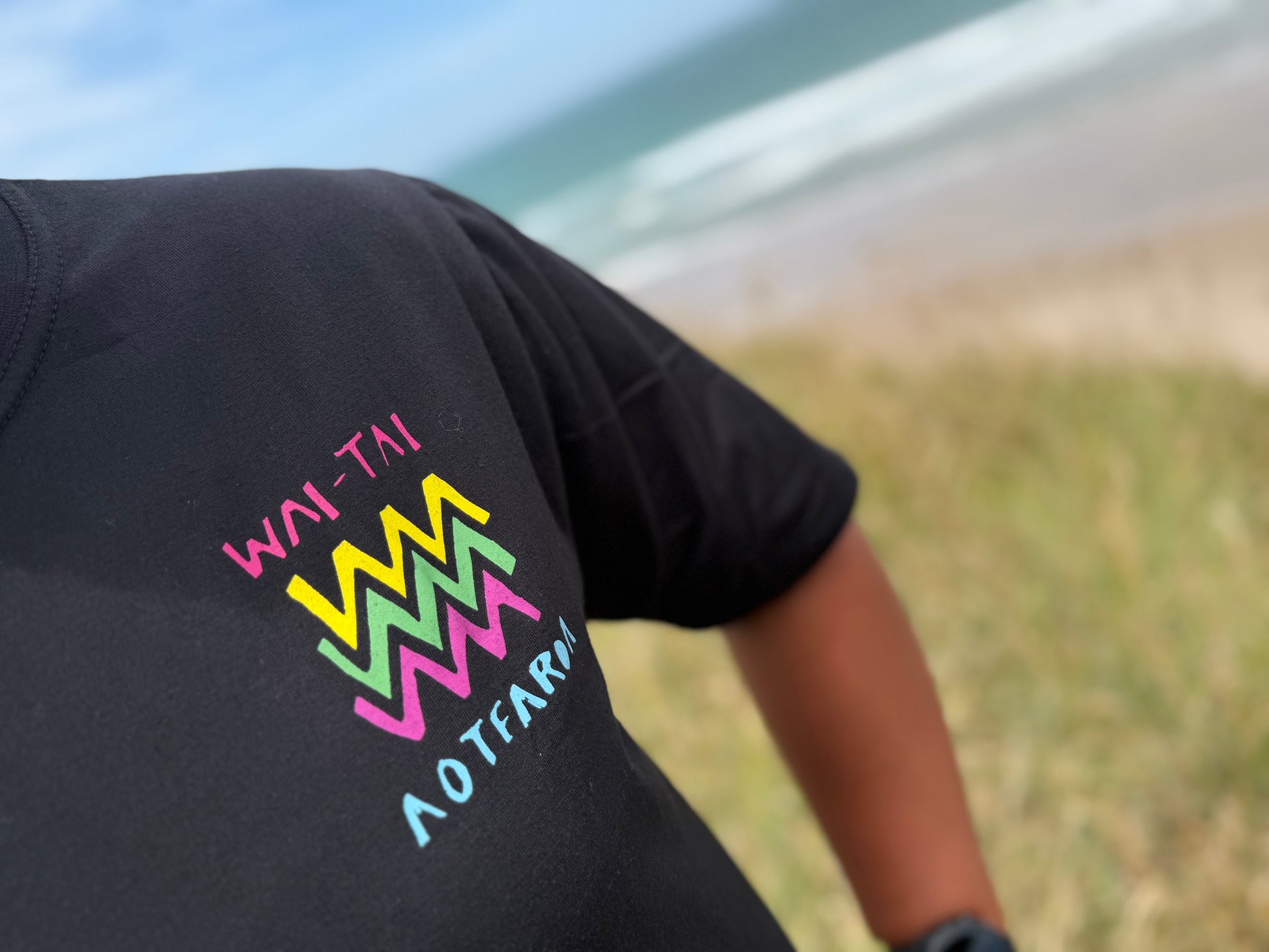 Wai-Tai Aotearoa Ono Whitu Black Unisex Maori Design T-Shirt in black worn by Hine Brooking showing bright design from front