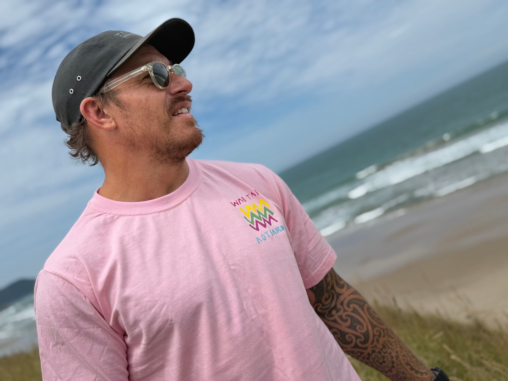 Wai-Tai Aotearoa Ono Whitu Pink Unisex Tee from frontshowing bright logo on Maia Gibbs at the beach