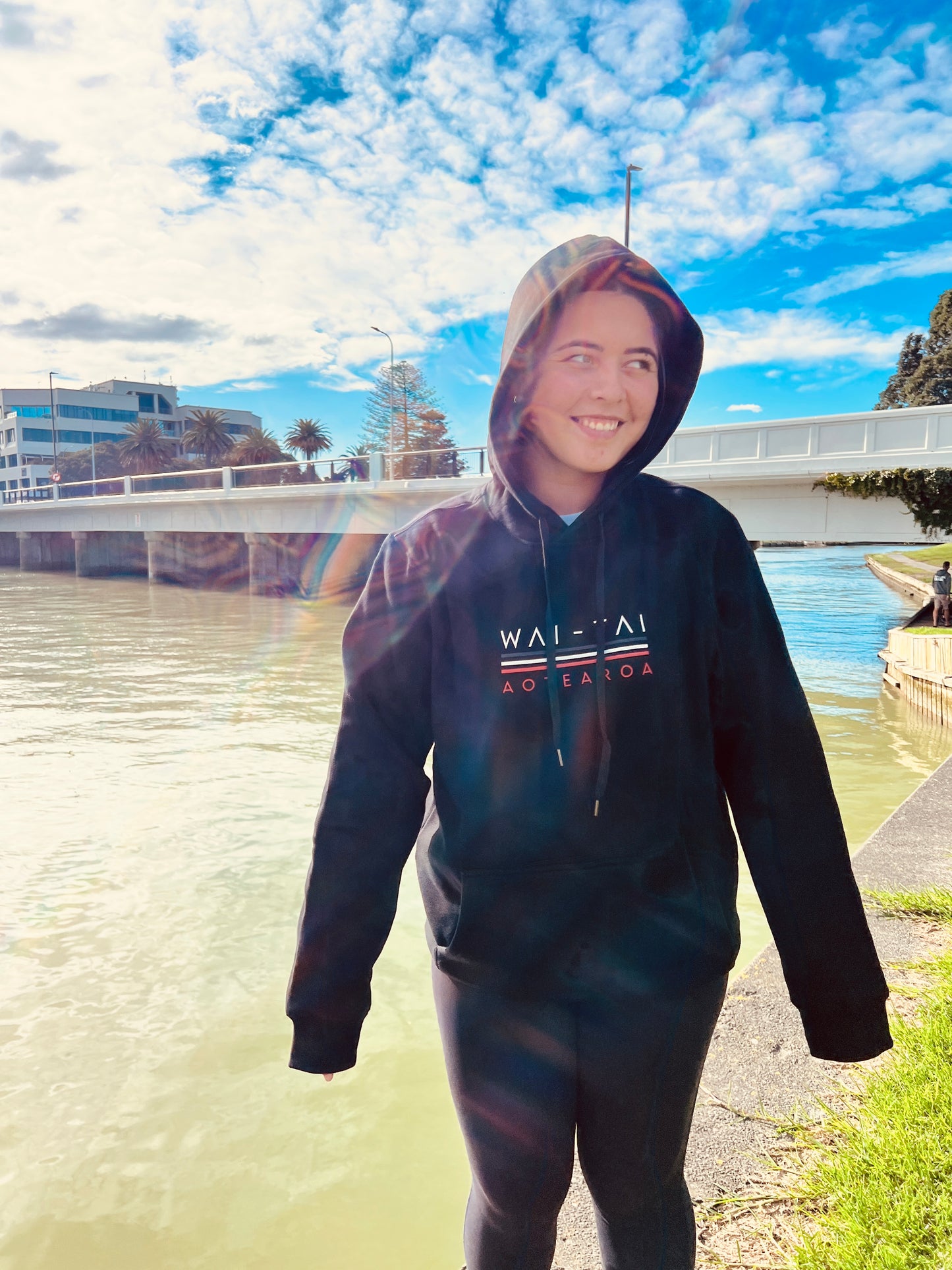 Wai-Tai Tipua Blackout Heavyweight Maori Design Unisex Hoodie in black from the front by river in Gisborne