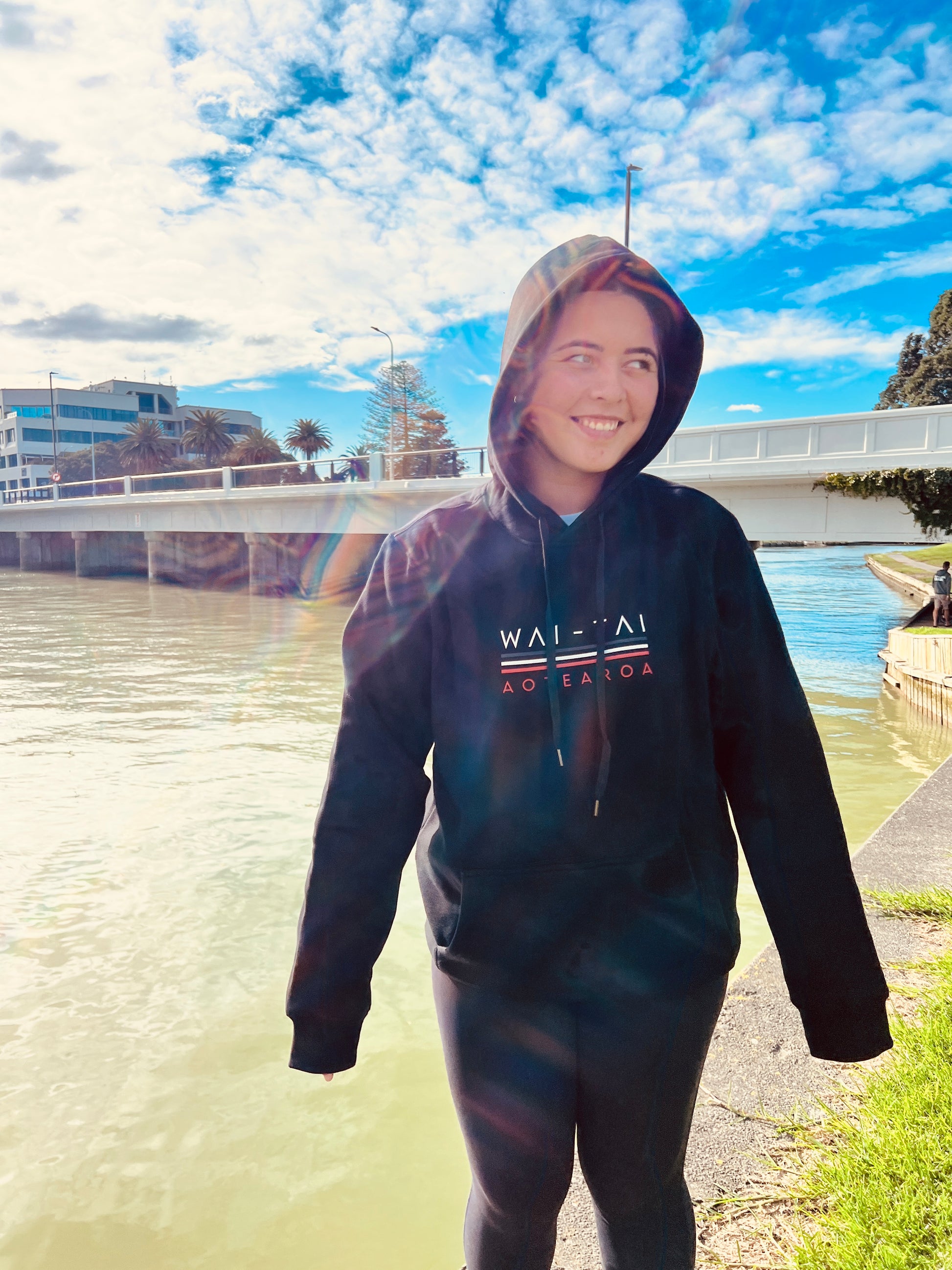 Wai-Tai Tipua Blackout Heavyweight Maori Design Unisex Hoodie in black from the front by river in Gisborne