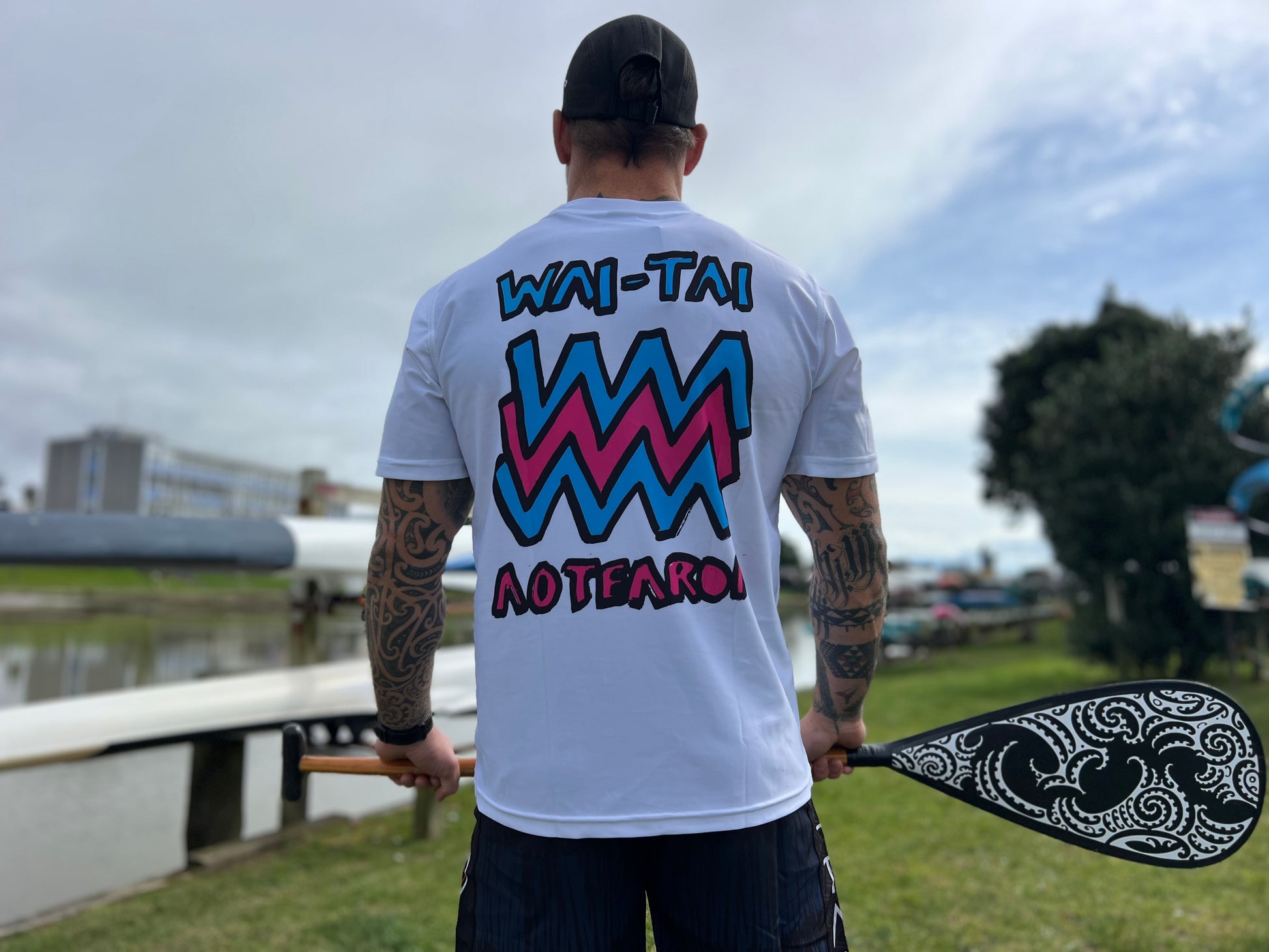 Wai-Tai Aotearoa Mura Rash Tee in white on Maia Gibbs holding a paddle in Gisborne from the back view