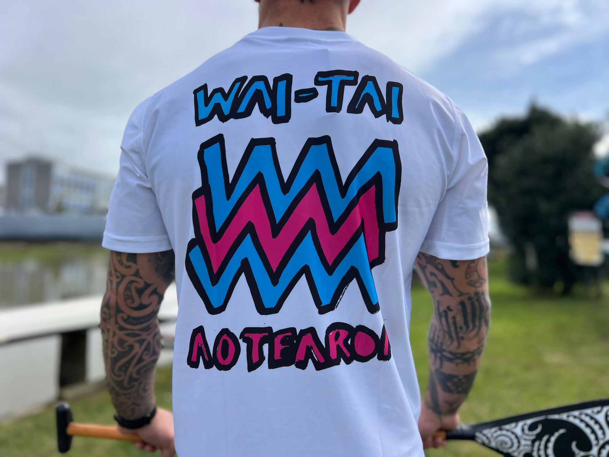 Wai-Tai Aotearoa Mura Rash Tee in white on Maia Gibbs holding a paddle in Gisborne from the back view close up