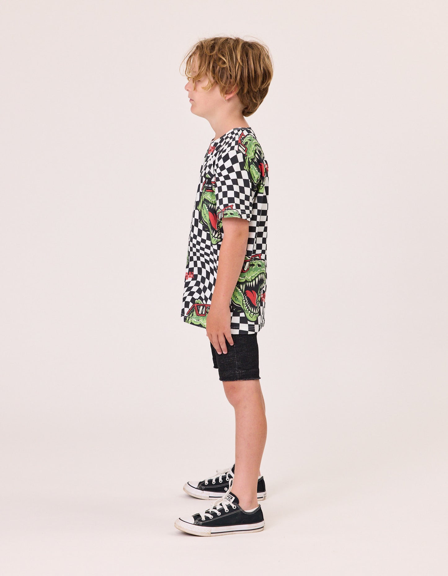 Radicool T-Rex Twisted Chequer Tee
 in black and white checkered with t-rex head imagery on model from the side