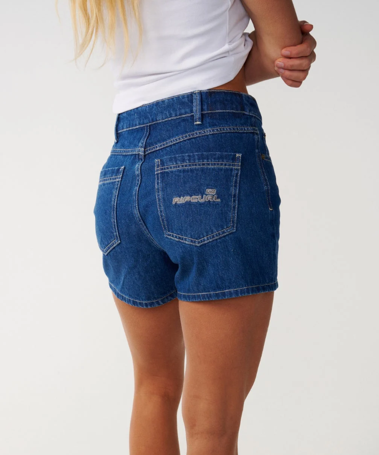 Rip Curl Tabby Women's Denim Shorts in mid blue on model in white tee from the back showing Rip Curl embroidery on pocket