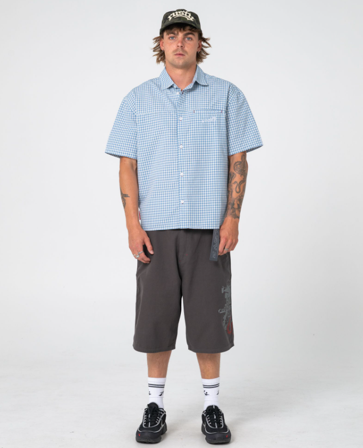 Rusty Stasher 25" Baggy Canvas Walkshorts in carbon colourway on model in blue checked shirt and Rusty cap