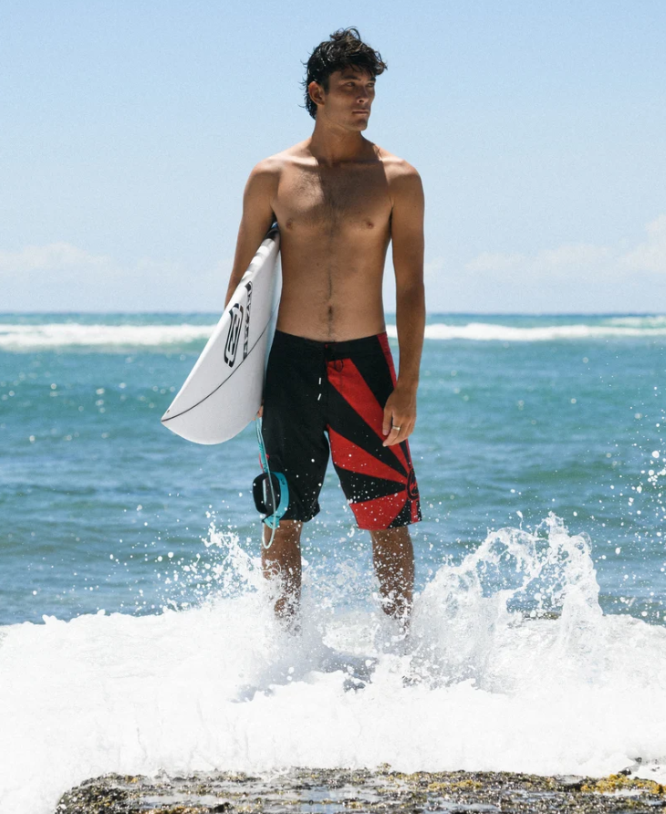 Billabong A.I Rising Sun Pro Boardshorts in black and red on surfer holding surfboard