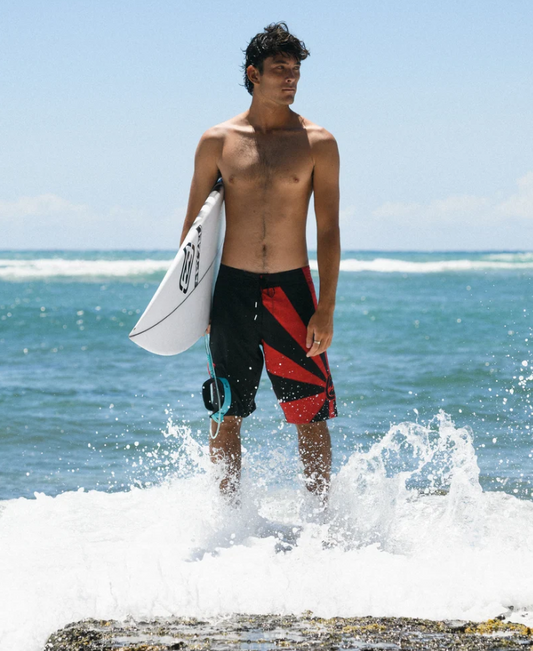 Billabong A.I Rising Sun Pro Boardshorts in black and red on surfer holding surfboard