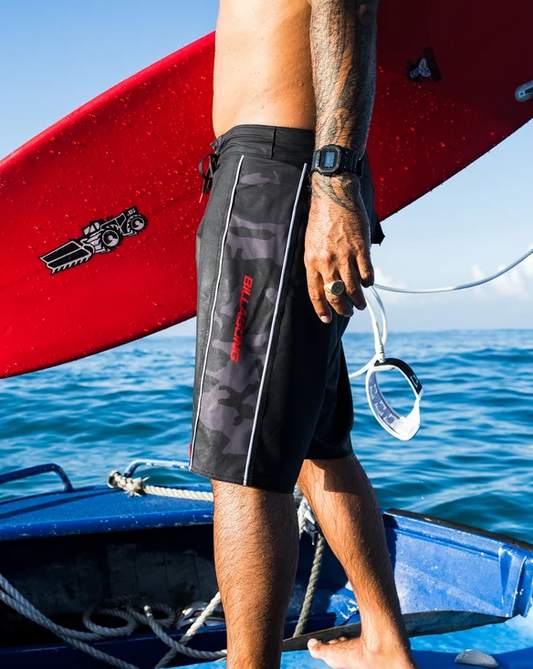 Billabong Adiv Strike Mission DBah 21" Boardshorts in black with camo paneling on model carrying red surfboard from the side