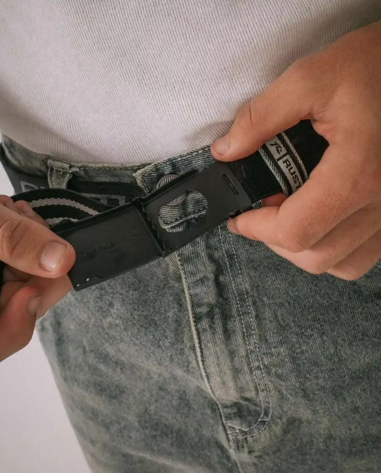 Rusty Flip Daddy Reversible Elastic Webbing Belt in black in model's jeans showing buckle close up