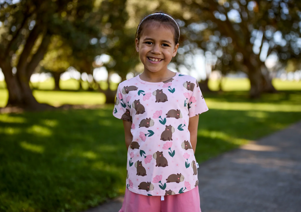 Kissed By Radicool Floral Capybaras Girls Tee in pink on a girl in the park