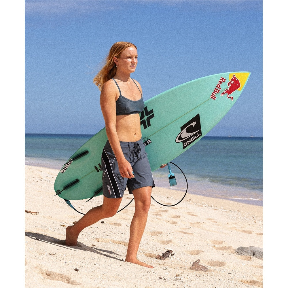 O'Neill Y2K Superfreak 7" Women's Boardshorts in slate colourway on surfer carrying her surfboard at the beach