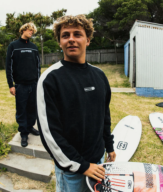 Billabong Spec Bio Pill Men's Crew in black with white detail on model holding surfboard