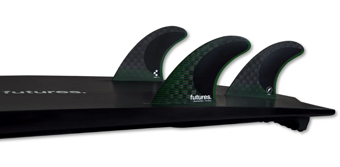 Futures F8 Blackstix Neutral Thruster Fin Set (large) in black and green in the back of a black surfboard
