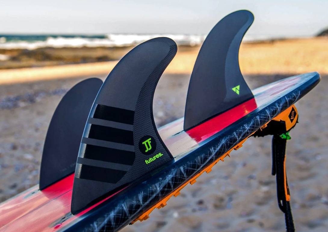 Futures JJF Alpha Surfboard Fin Set in blakc with green decals in back of a surfboard