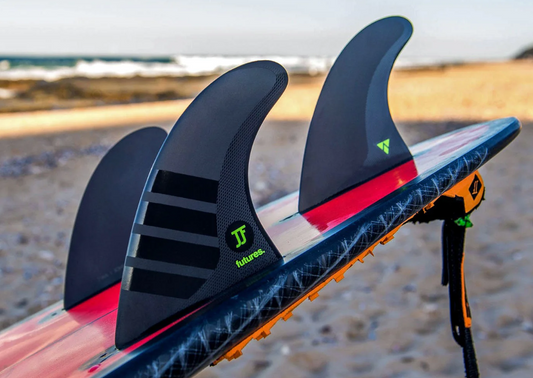 Futures JJF Alpha Surfboard Fin Set in blakc with green decals in back of a surfboard