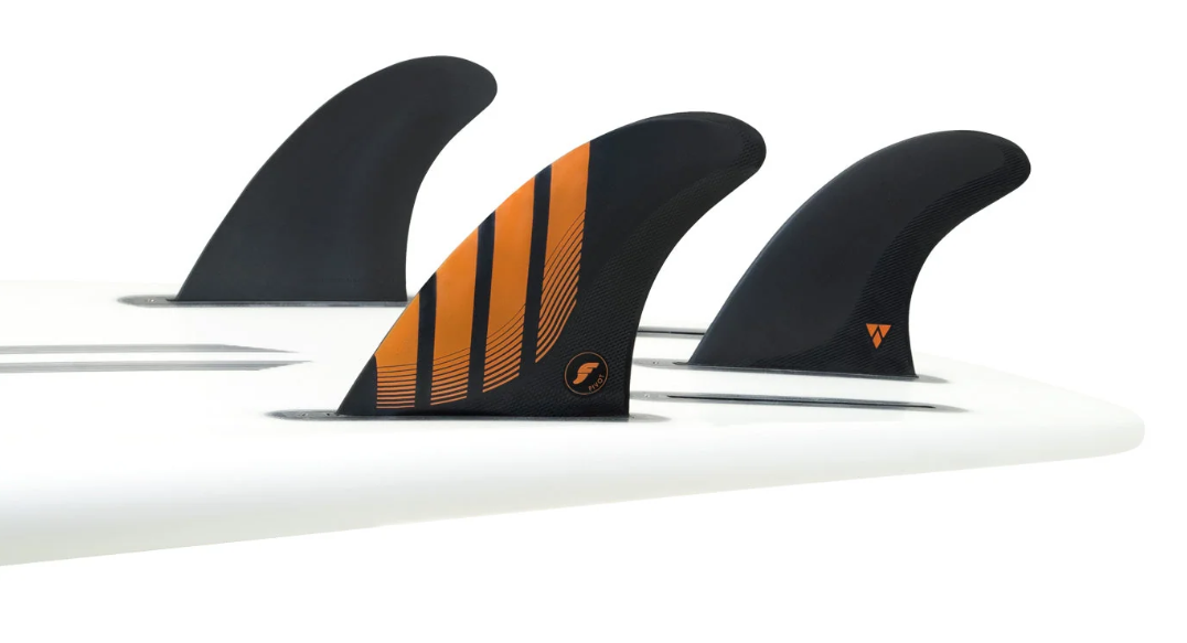 Futures Fins Pivot Alpha Carbon Thruster Fins in black with orange, medium set of fins in the tail of a surfboard